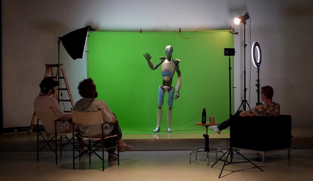 Set di chroma key verde con attore in tuta motion capture, softbox di scena e tecnici seduti che osservano